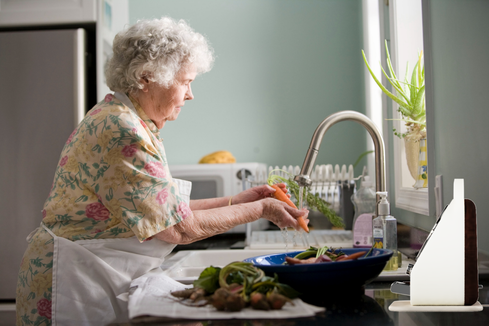 Elderly lady with early onset dementia cooking in the kitchen with her Connect device playing music or playing videos of family etc. 