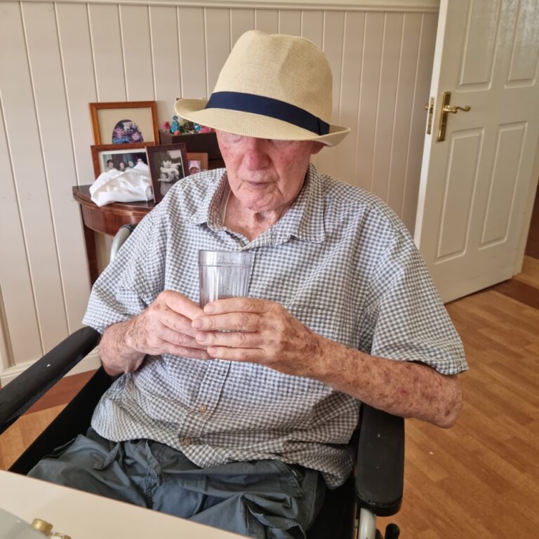 Eldery person with dementia sitting drinking water while they listen to Connect on the tray in front of them.